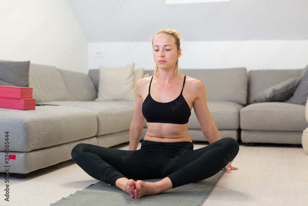 Beautiful blonde woman doing home workout indoors. Woman practice yoga at home. Fit girl using workout tutorials for healthy active lifestyle. Woman using quarantine for home workouts. Stretching Beautiful blonde woman doing home workout indoors. Woman practice yoga at home. Fit girl using workout tutorials for healthy active lifestyle. Woman using quarantine for home workouts. Stretching