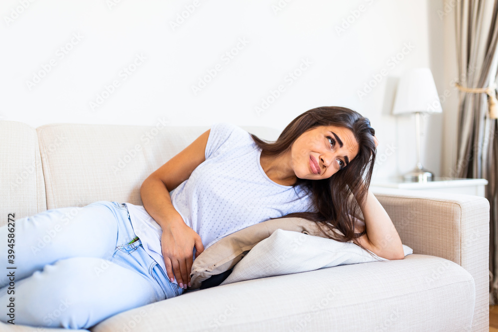 Woman in painful expression holding hands against belly suffering menstrual period pain,sitting sad on home bed, having tummy cramp in female health concept Woman in painful expression holding hands against belly suffering menstrual period pain,sitting sad on home bed, having tummy cramp in female health concept