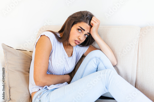 Woman in painful expression holding hands against belly suffering menstrual period pain, lying sad on home bed, having tummy cramp in female health concept