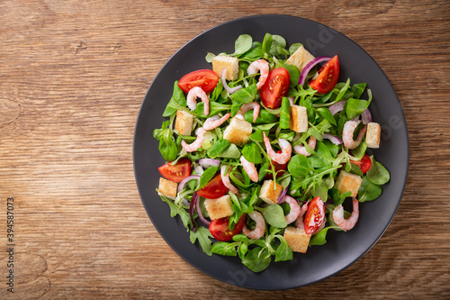 plate of fresh salad with shrimps, greens and tomato on a wooden table