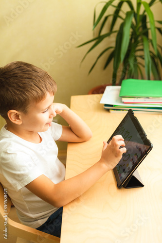Happy boy doing homework with tablet at home. Child using gadgets for study. Education and distance learning concept