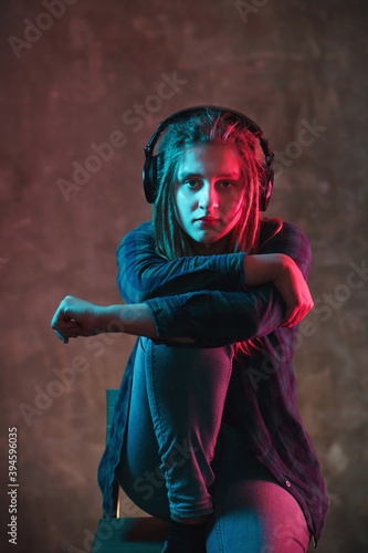 Girl with dreadlocks in headphones with colorful neon lighting on dark background. Stylish young woman in futuristic environment.