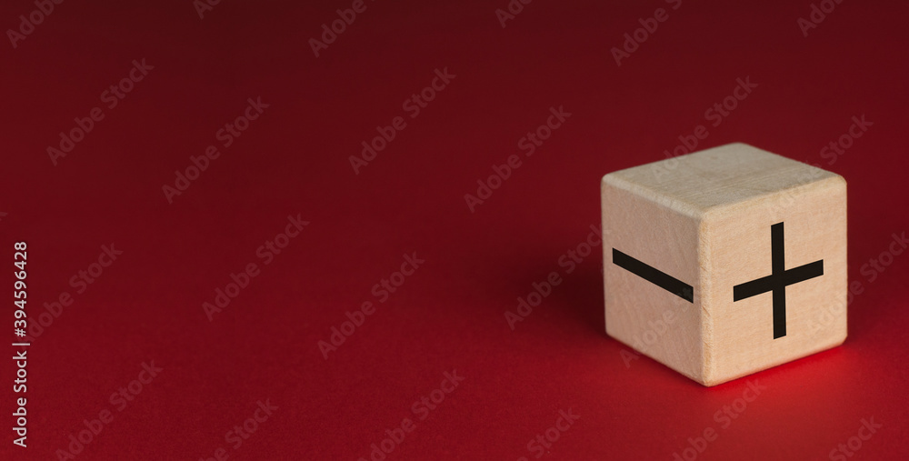 Wooden cube on a red background. + and - inscription on the cube. Wooden cube on a red background. + and - inscription on the cube.