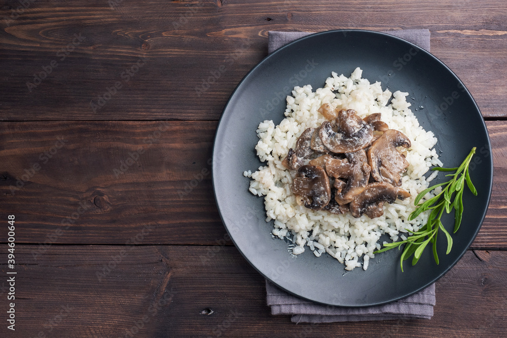 Risotto with mushrooms on a black plate. Boiled white rice with champignons in cream sauce. Dark wooden background. Copy space Risotto with mushrooms on a black plate. Boiled white rice with champignons in cream sauce. Dark wooden background. Copy space