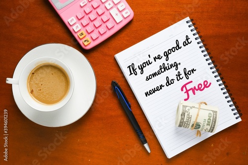 A notebook word written "If you're good at something, never so it for free" with coffee, fake money and calculator insight.