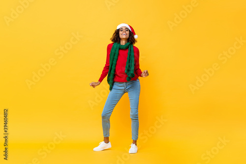 Fun portrait of happy African American woman in Christmas attire dancing on isolated yellow studio background