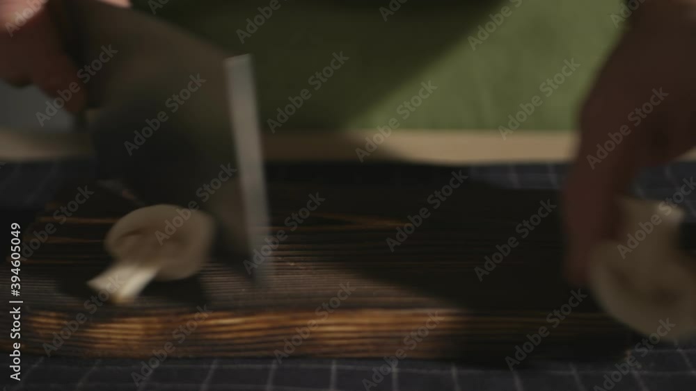 a cook in a green apron is cutting a champignon mushroom on a brown board with a large kitchen knife. Man preparing eco food a cook in a green apron is cutting a champignon mushroom on a brown board with a large kitchen knife. Man preparing eco food