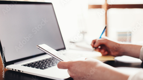 Woman working and writing with the pen, mobile phone and laptop computer. Remote studiyng from home. Lockdown business. Hands close-up wide screen