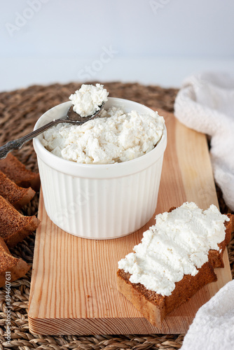 Fresh ricotta cheese in white ceramic bowl with rye sandwich on wooden cutting board photo