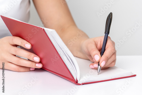 Young female hand writes notes to notebook planning her schedule at white table