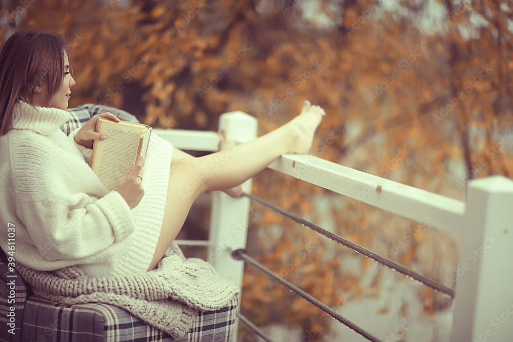 Naklejka premium girl in a knitted sweater reads a book on the veranda in the park, seasonal romance concept