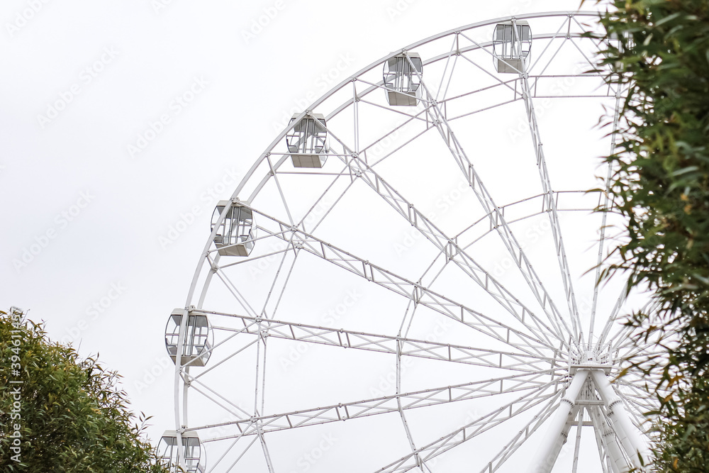 Modern white Ferris wheel in the central park against sky. Entertainment, attraction, amusement park, minimal concept or background. Modern white Ferris wheel in the central park against sky. Entertainment, attraction, amusement park, minimal concept or background.