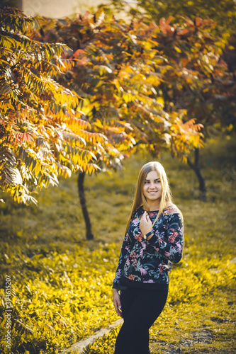 Woman girl long-haired blonde in an alley with trees with red leaves. She is happy confident in a photo shoot. Autumn park sunny warm day.