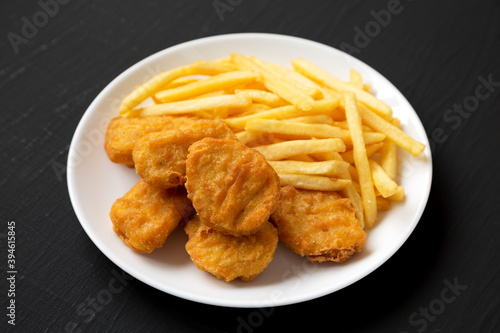 Tasty Fastfood: Chicken Nuggets and French Fries on a plate on a black background, side view.