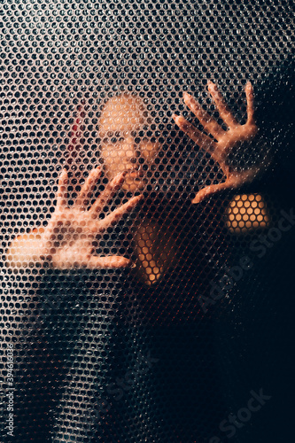 Mysterious woman. Black magic. Esoteric practice. Textured portrait of female fortune teller silhouette touching plastic bubble wrap wall with hands in darkness.