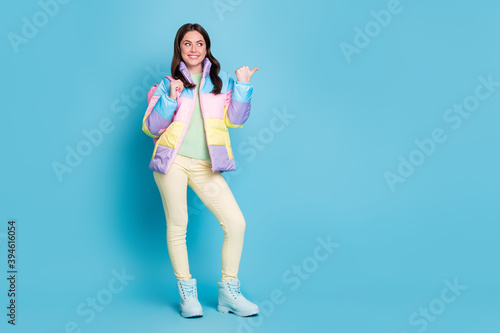 Full length photo portrait of dreamy woman with pink bag pointing thumb looking at blank space isolated on pastel blue colored background © deagreez