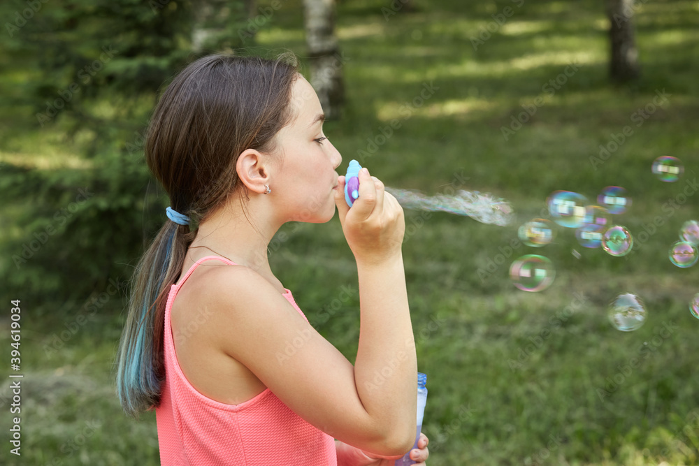Girl on summer vacation playing in nature and blowing soap bubbles. Sunny summer warm day.