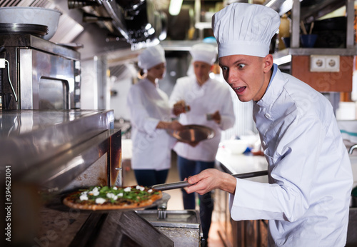 Portrait of happy surprised chef getting ready pizza out of professional oven in modern restaurant kitchen
