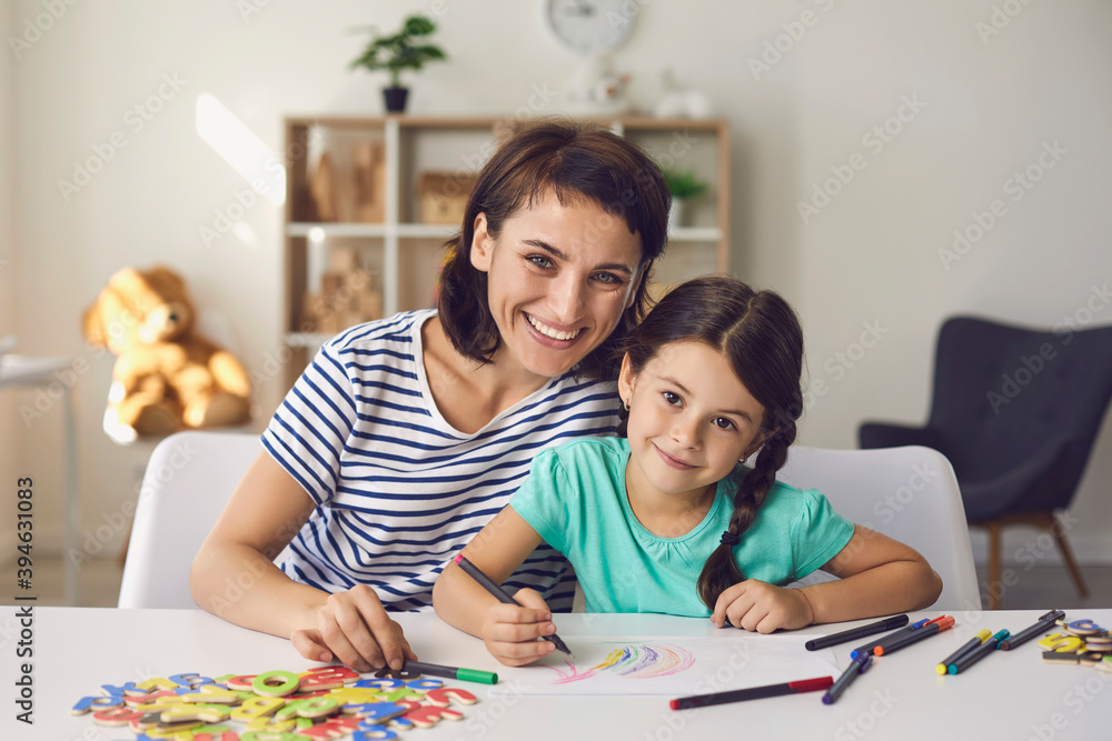 Beautiful mom and preschool girl draw with felt-tip pens and smile at the camera.