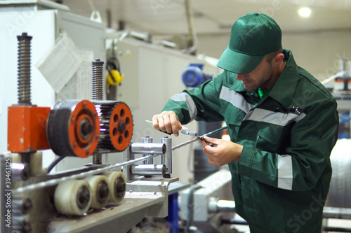 factory worker in a robe and cap checks the performance of the device for the production of cable products from a copper core