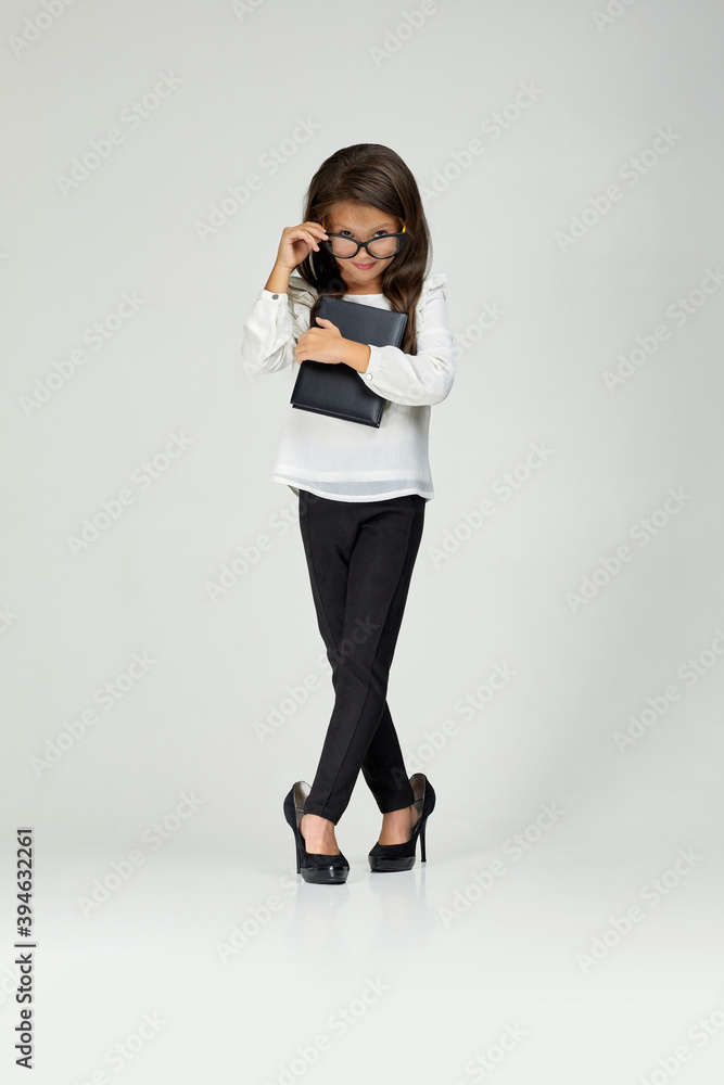 cute little child girl in oversized mother's shoes and glasses holding notebook on white background. child playing businesswoman cute little child girl in oversized mother's shoes and glasses holding notebook on white background. child playing businesswoman