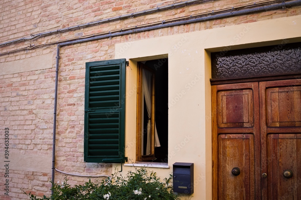 A facade of an old traditional italian house with an open window and a wooden door (Corinaldo, Italy, Europe)