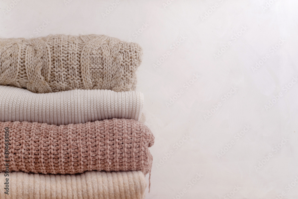 Stack of knitted sweaters in pastel colors with different patterns of knitting on a white background. Warm folded winter clothing. Close up, copy space.