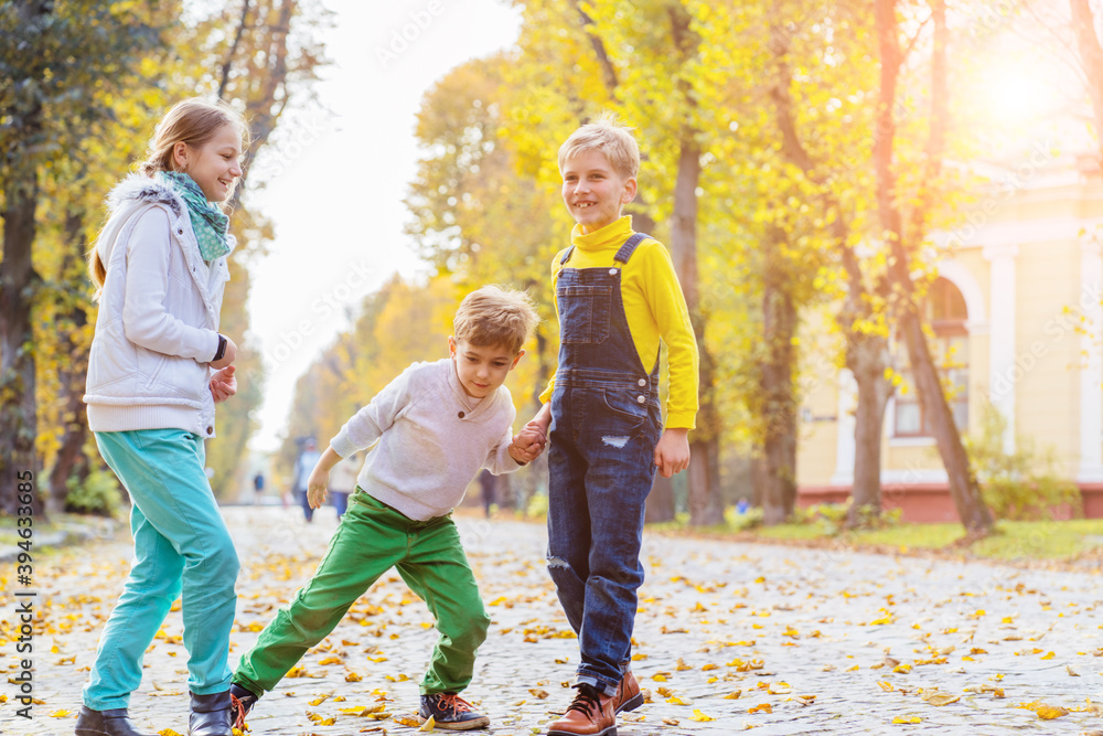Fototapeta premium Children girl and two boys playing with soap bubbles, someone blows children catch bubbles. Beautiful natural landscape, autumn park on background, happy childhood.