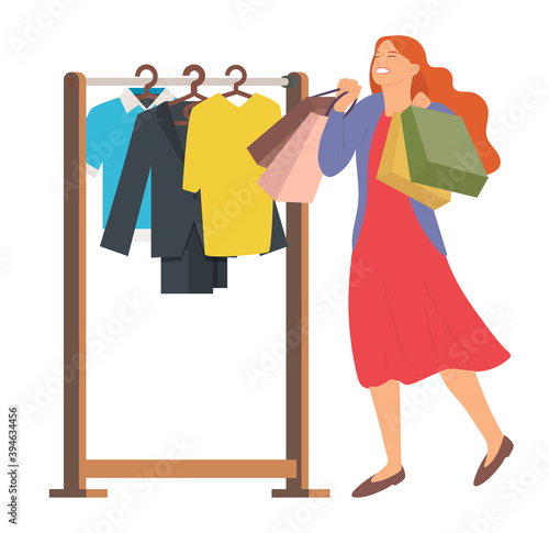 Woman with shopping bags. Young beautiful happy girl picks up multi-colored packages. Female character is choosing outfit to wear. Clothes fitting. Hanger with items of clothing on the background