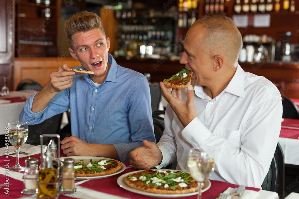 Two male friends enjoying delicious pizza in cozy restaurant..