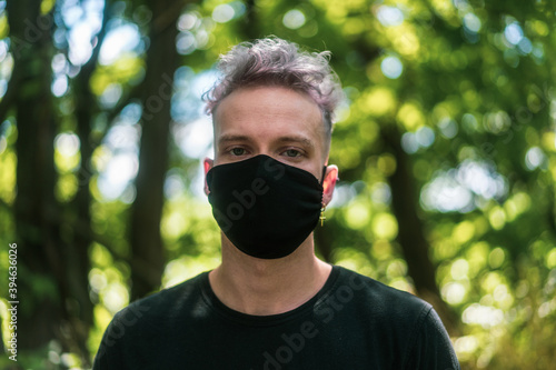 portrait of young man with white hair wearing a black face mask in forest in summer during corona