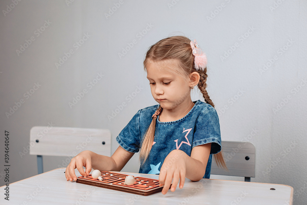Portrait of an adorable beautiful cute child sitting at a white table and solving a puzzle. Focus concept. photo with noise