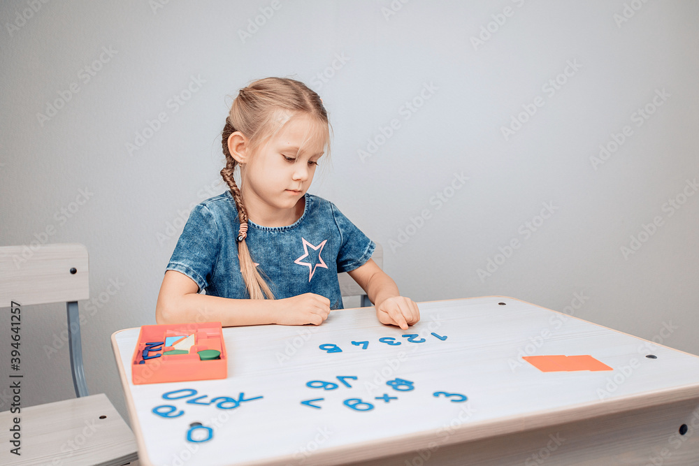 Portrait of a focused intelligent cool child sitting at a white table with numbers in the correct order and a girl pointing to the numbers, memorizing them. Development process. Study concept.