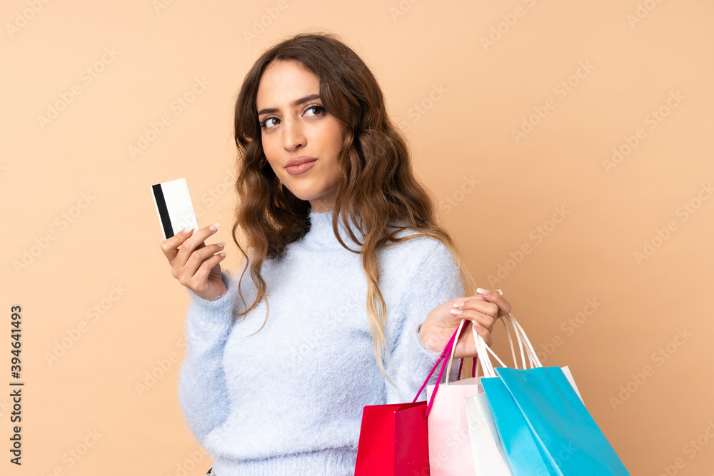 Young woman over isolated background holding shopping bags and a credit card and thinking Young woman over isolated background holding shopping bags and a credit card and thinking