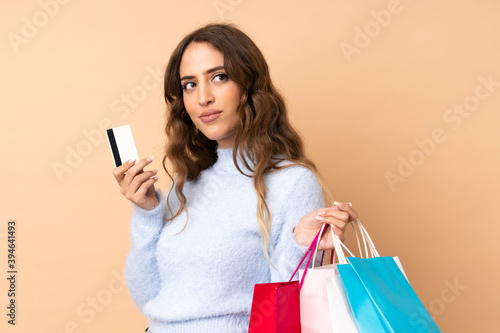 Young woman over isolated background holding shopping bags and a credit card and thinking