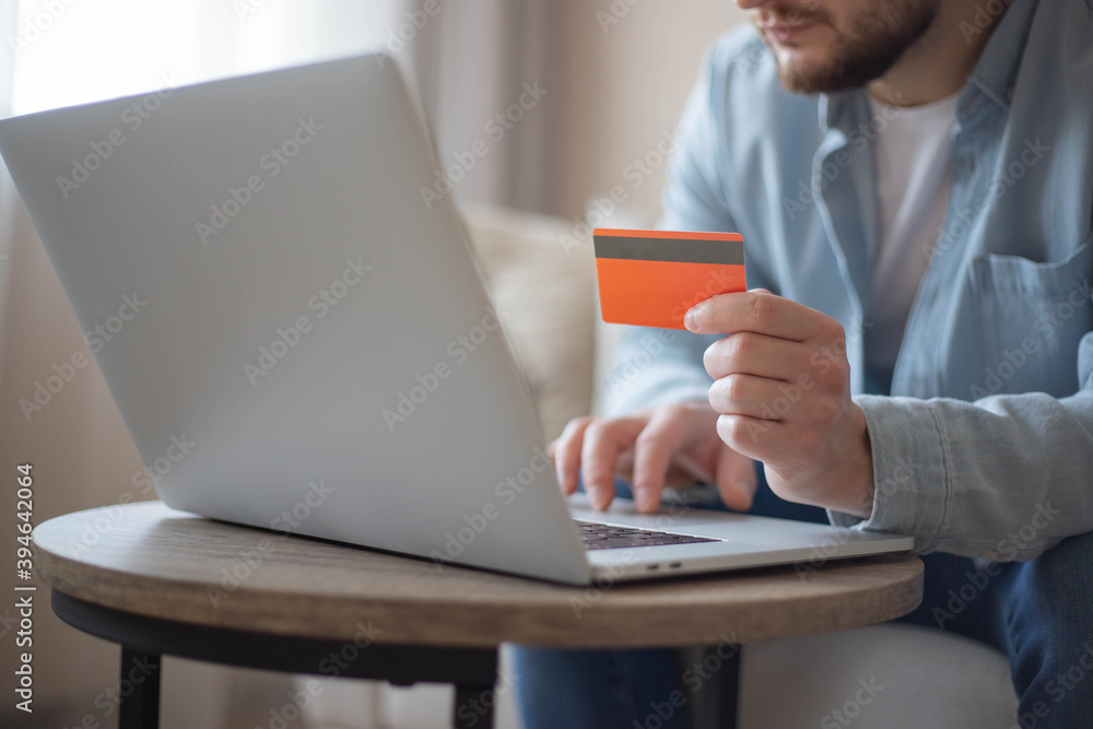 Businessman holding plastic credit card in hand and using laptop computer while sitting at the wooden table.Man making online money transfer. Online shopping. Businessman holding plastic credit card in hand and using laptop computer while sitting at the wooden table.Man making online money transfer. Online shopping.