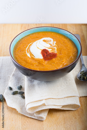 An orange pumpkin soup in a bowl on a linen cloth with pumpkin seeds and a spoon