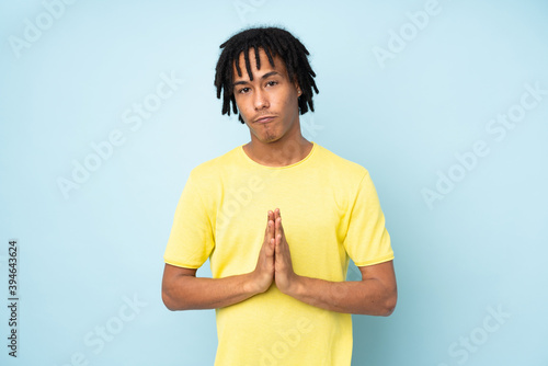 Young african american man isolated on blue background keeps palm together. Person asks for something