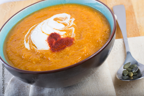 An orange pumpkin soup in a bowl on a linen cloth with pumpkin seeds and a spoon