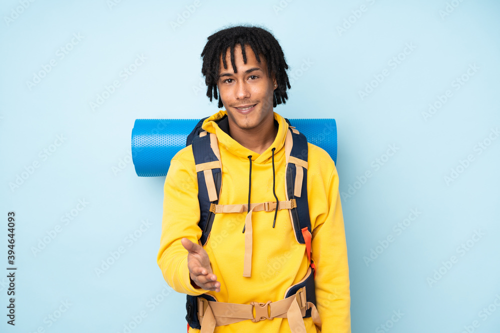 Young mountaineer african american man with a big backpack isolated on a blue background handshaking after good deal Young mountaineer african american man with a big backpack isolated on a blue background handshaking after good deal