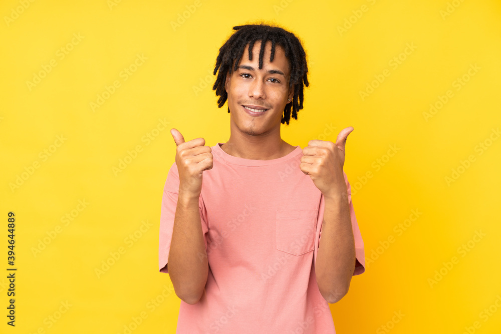 Young african american man isolated on yellow background with thumbs up gesture and smiling Young african american man isolated on yellow background with thumbs up gesture and smiling