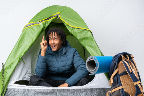 Young african american man inside a camping green tent intending to realizes the solution while lifting a finger up