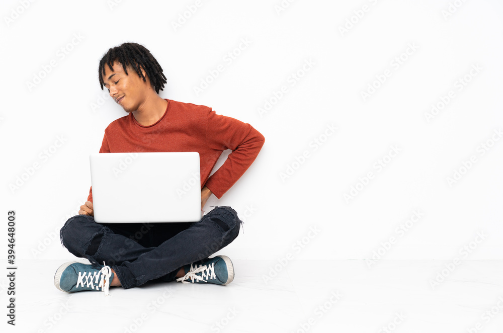 Young african american man sitting on the floor and working with his laptop suffering from backache for having made an effort Young african american man sitting on the floor and working with his laptop suffering from backache for having made an effort