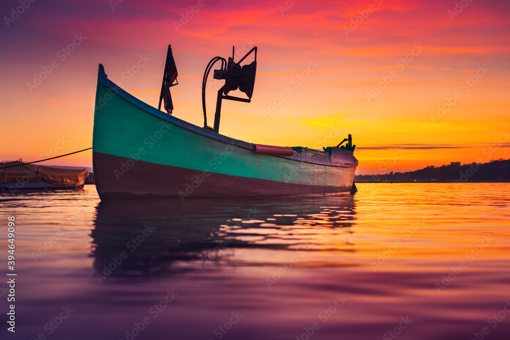 Fishing boat on sea shore and dramatic colorful sunset