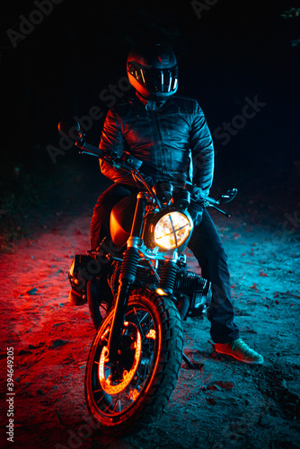 biker with black helmet sitting on his bike at night and colorful lights 