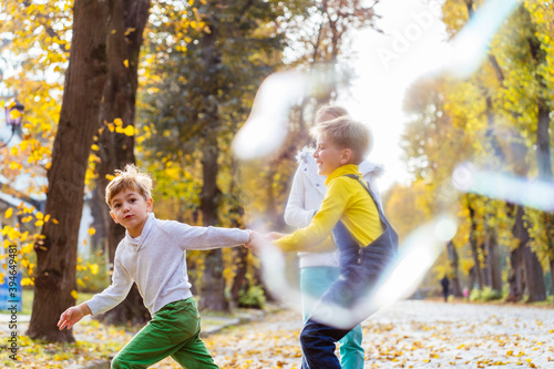 Children girl and two boys playing with soap bubbles, someone blows children catch bubbles. Beautiful natural landscape, autumn park on background, happy childhood.