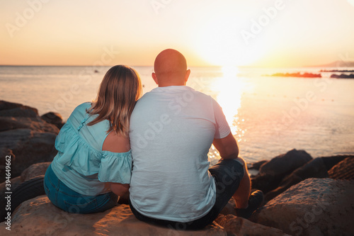 An adult couple, a plus-size man and woman, sit on the beach, watching the sunset over the ocean. Rear view. The concept of Valentine's day