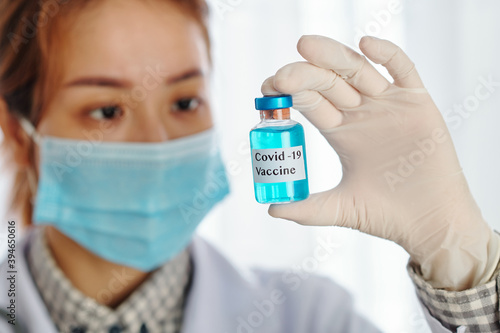 Vial with blue covid-19 vaccine in hands of serious young Asian laboratory worker