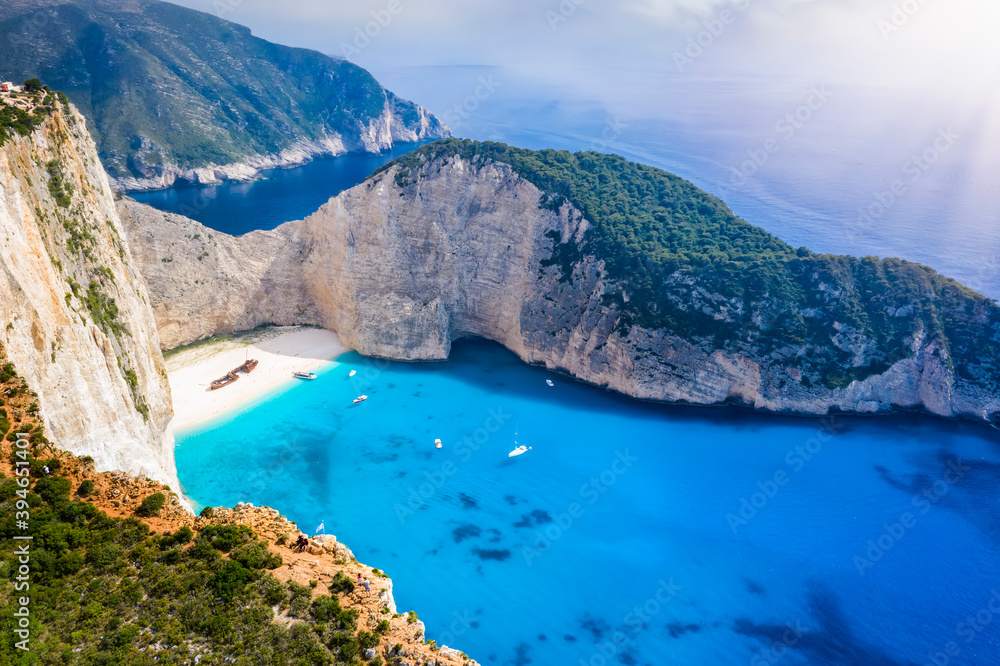 Aerial view to the fluorescent, blue sea of the popular Navagio shipwreck beach on the Greek island of Zakynthos on a summer day with low clouds