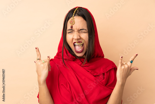 Young Indian woman isolated on beige background making horn gesture